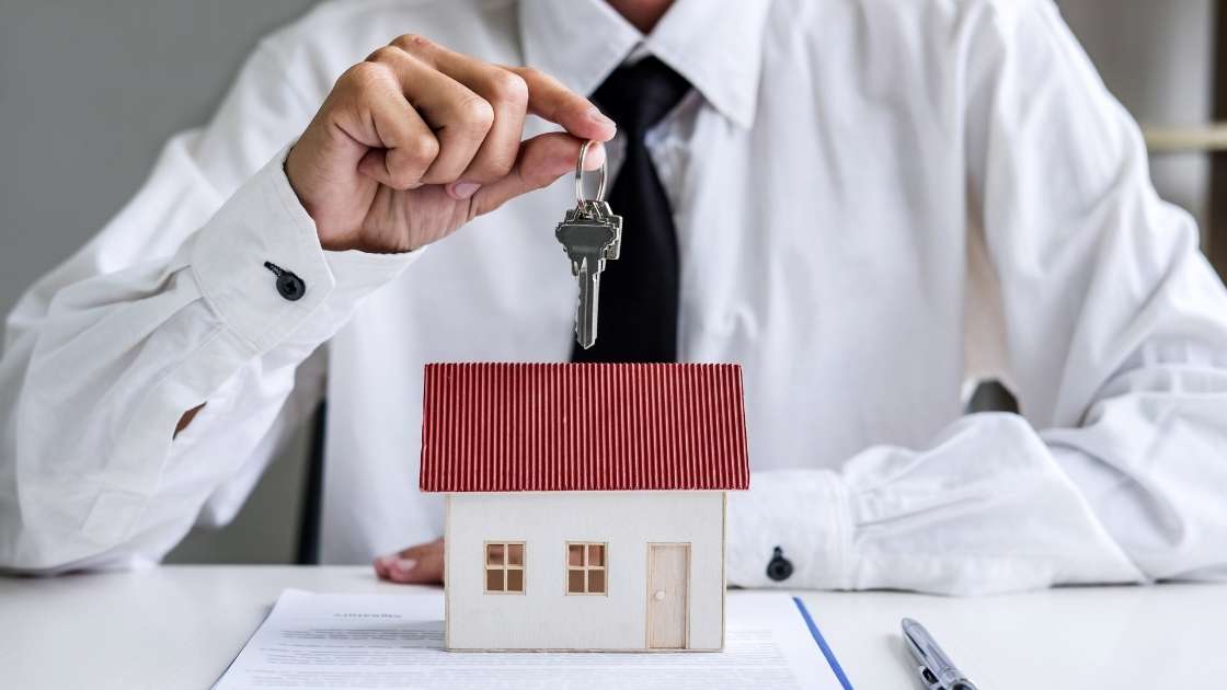 person-wearing-a-dress-shirt-and-tie-holding-a-set-of-house-keys-above-a-figurine-house