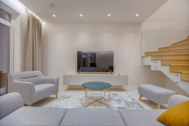 neutral living room with grey couch facing a TV screen with orange accent pieces